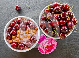 Breakfast bowl with yogurt, granola or muesli or oat flakes, fresh cherries and nuts. Black stone background, pink rose flower