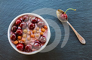 Breakfast bowl with yogurt, granola or muesli or oat flakes, fresh cherries and nuts. Black stone background, top view