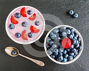 Breakfast bowl with yogurt, muesli, fresh blueberries and strawberries. Black stone background, top view