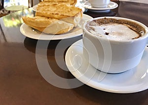 Breakfast at Brazil with french bread toasted with butter on the plate with capuccino on table