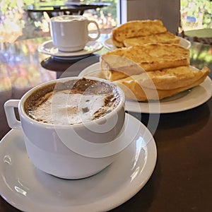 Breakfast at Brazil with french bread toasted with butter on the plate with capuccino on table