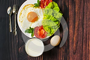 Breakfast with bread, fried eggs, milk and vegetables and fried tomato pieces on wood background.