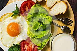 Breakfast with bread, fried eggs, milk and vegetables and fried tomato pieces on wood background.