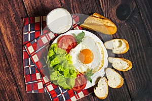 Breakfast with bread, fried eggs, milk and vegetables and fried tomato pieces on wood background.