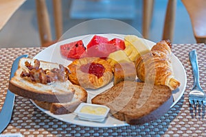 Breakfast with bread slices , fruits , croissant , butter and strawberry jam