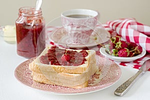 Breakfast of bread toasts with butter and strawberry-rhubarb jam, served with tea. Rustic style.