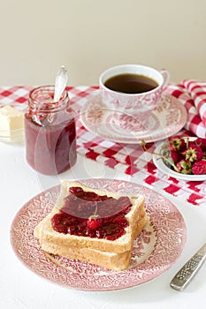 Breakfast of bread toasts with butter and strawberry-rhubarb jam, served with tea. Rustic style.