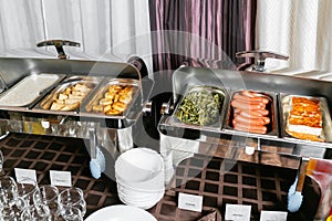 Breakfast buffet in hotel. Lots of heated trays ready for service. Metal containers with warm meals