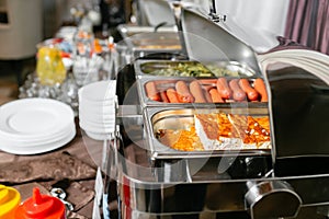 Breakfast buffet in hotel. Lots of heated trays ready for service. Metal containers with warm meals