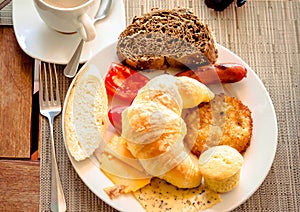 Breakfast at cafe with croissant, bread, cheese, tomatoes on plate.
