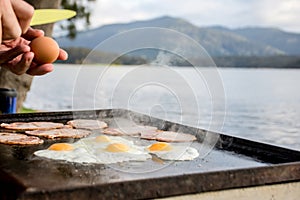 Breakfast camp cooking, Grilling eggs and bacon on the bbq plate with beautiful nature landscape