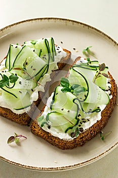 Breakfast, cereal bread sandwiches, cream cheese, sliced cucumber, with micro greenery on a light table, close-up, top