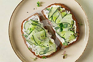 Breakfast, cereal bread sandwiches, cream cheese, sliced cucumber, with micro greenery on a light table, close-up, top