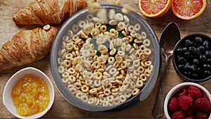 Breakfast cereal rings fall into the ceramic bowl. Placed on wooden table