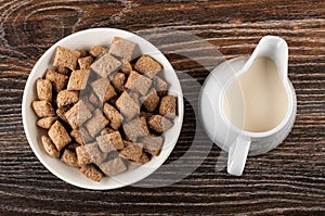 Breakfast cereals with filling in bowl, pitcher with baked milk on wooden table. Top view
