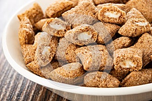 Breakfast cereals, halves of pillows with dairy filling in bowl on wooden table