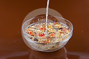 Breakfast cereals, oatmeal with candied fruits and nuts in a glass bowl and pouring milk, brown background
