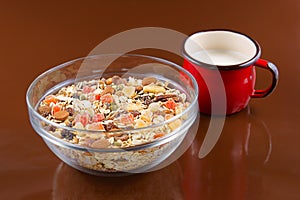 Breakfast cereals, oatmeal with candied fruits and nuts in a glass bowl and red cup milk, brown background