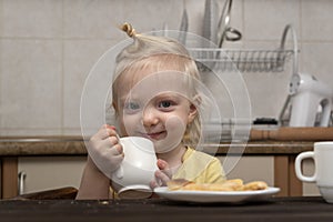 Breakfast with child. Little girl drinks a milk. Cute blonde child with cup in hands in kitchen