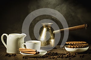 Breakfast with coffee and cookies/coffee cup with cinnamon, old pot, creamer and chocolate cookies on a wooden table. Against