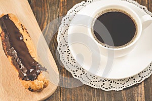 breakfast with coffee cup and eclair/coffee cup and eclair on a wooden table. Top view