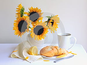 Breakfast coffee with fresh bread and lemon on white tablecloth with beautiful sunflowers in white vase.