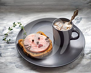 Breakfast with coffee and funny sandwich with sausage in the form of a cat`s face on a dark plate on a dark background in