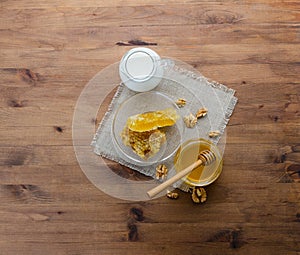 Breakfast composition with fresh honey, dipper, honeycomb, milk and nuts on wooden background