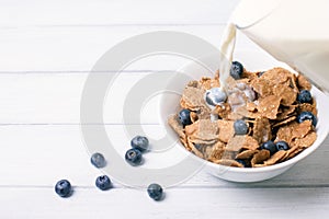 Breakfast with corn flakes with fresh berries and pouring milk on white wooden background. Selective focus and shallow depth of