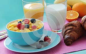 Breakfast with corn flakes, milk, croissants, orange juice and fresh fruits as banana, oranges and berries.