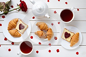 Breakfast for couple on Valentines Day with toasts, heart shaped jam, croissants, red rose flower, petals and tea