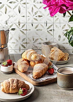 Breakfast with croissants, coffee, berries, peonies flower, honey composition with tile background