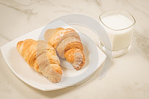 breakfast with croissants and milk/croissants in a plate and glasses milk on a white marble table