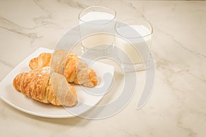 Breakfast with croissants and milk/croissants in a plate and glasses milk on a white marble table. Copy space