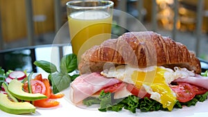 breakfast cut with a fork and knife egg on a croissant sandwich yellow yolk flows out in a stream avocado salad red