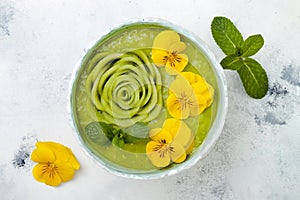 Breakfast detox green smoothie bowl topped with kiwi rose and edible Pansy flowers.