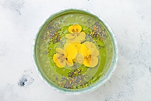 Breakfast detox green smoothie bowl topped with superfoods, chia seeds, bee pollen and edible flowers. Overhead, flat lay