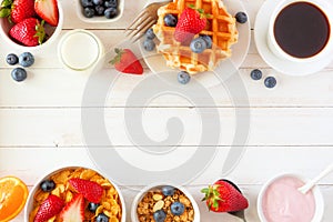 Breakfast double border of fruits, cereal, waffles, yogurt, milk and coffee. Top view over a white wood background.
