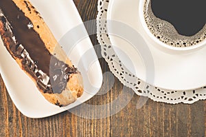 Breakfast with eclairs with chocolate and a coffee cup/breakfast with eclairs with chocolate and a coffee cup on a wooden