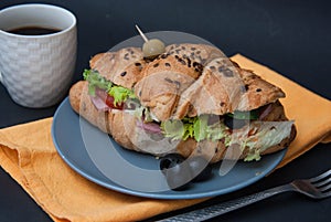 Breakfast Food with Coffee. Croissant Sandwich with Fried Eggs and Fresh Vegetables on Gray Plate with Orange Napkin over Dark Gra