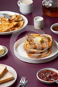 Breakfast food - plates with French toast with butter, crepes, toast bread, jam, honey, tea kettle, coffee cup, milk jug
