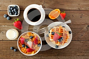 Breakfast food table scene. Fruits, cereal, waffles, milk and coffee. Top view over wood.