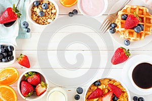 Breakfast frame of fruits, cereal, waffles, yogurt, milk and coffee. Top view over a white wood background.