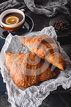 Breakfast with fresh french chocolate croissants on paper over dark background with napkin and cup of tea. Dessert
