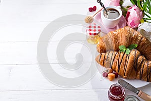 Breakfast freshly baked croissant decorated with jam and chocolate, flowers on wooden table in a kitchen with copy space