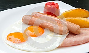 Breakfast with fried egg, sausages, tomato, potatoes fried on white plate