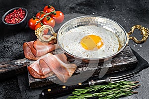 Breakfast with fried egg in a skilet with tomatoes and bacon. Black background. Top view