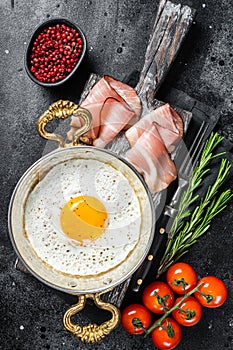 Breakfast with fried egg in a skilet with tomatoes and bacon. Black background. Top view photo