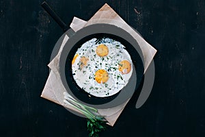 Breakfast. Fried eggs in cast iron frying pan on dark wooden background