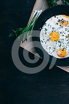 Breakfast. Fried eggs in cast iron frying pan on dark wooden background, vertical